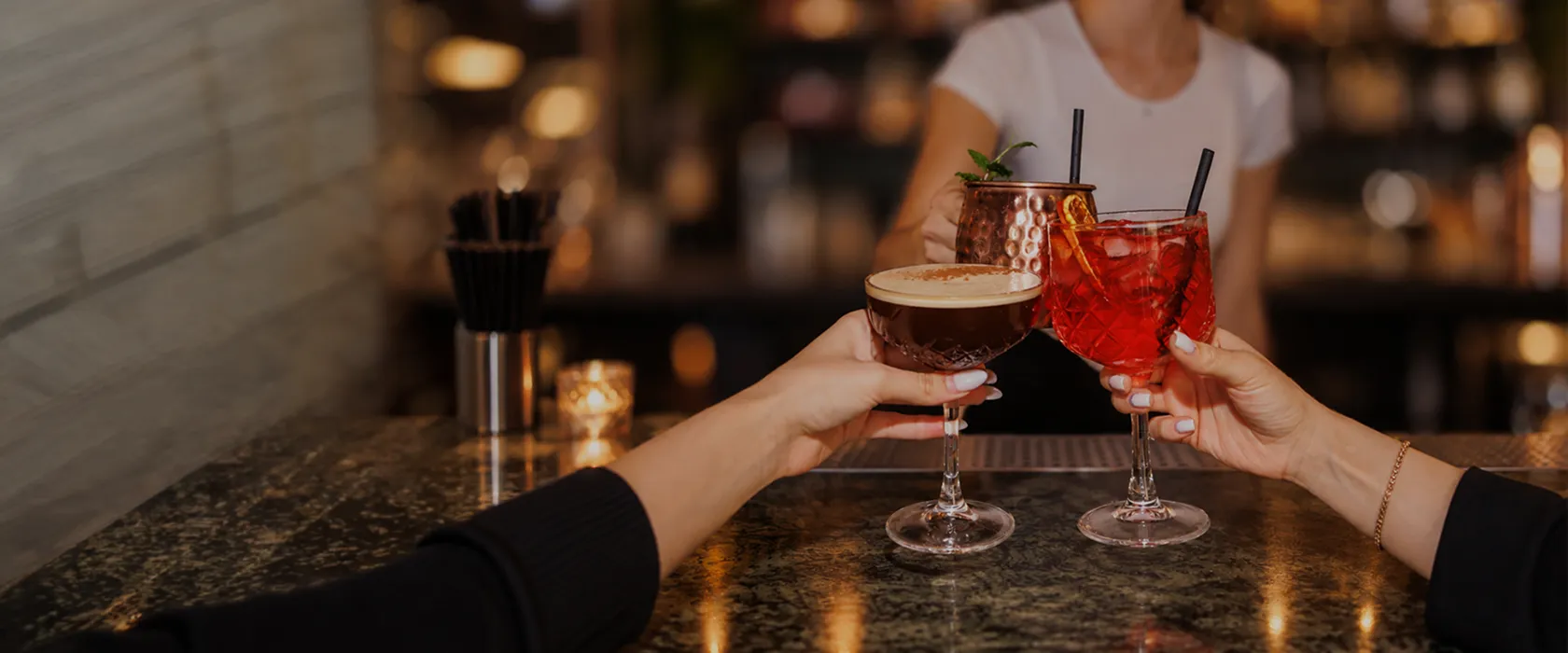Deux cocktails qui trinquent au comptoir d’un bar chaleureux et élégant