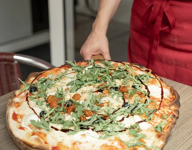 Pizza artisanale maison gratinée, garnie de roquette, mozzarella et tomates cerises