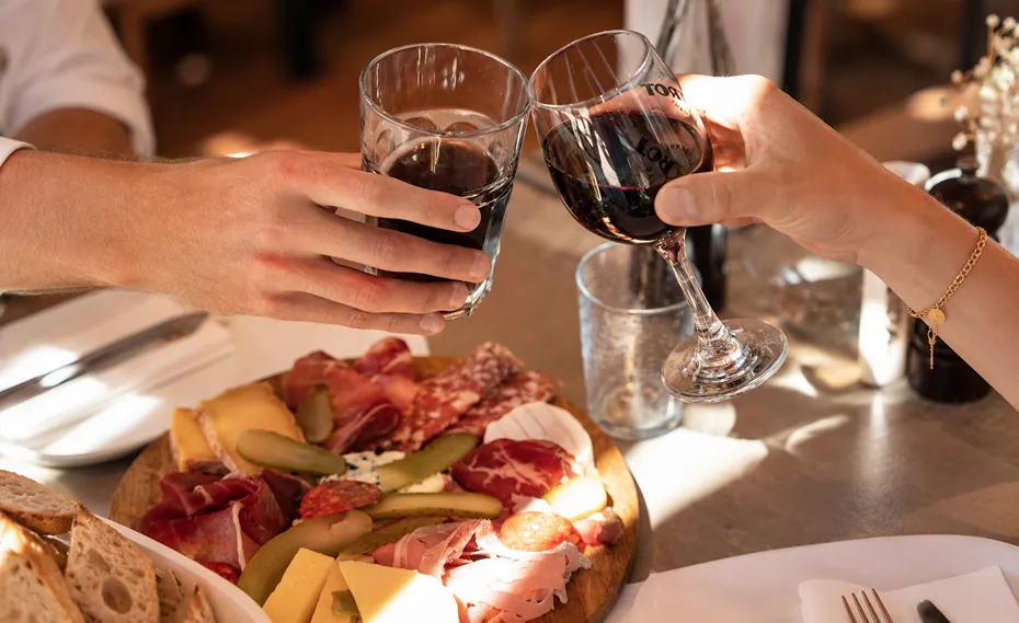 Deux verres de vin qui trinquent au-dessus d’une planche de charcuterie et de fromages artisanaux